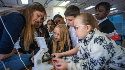 A crowd of primary-aged children huddle around a microscope