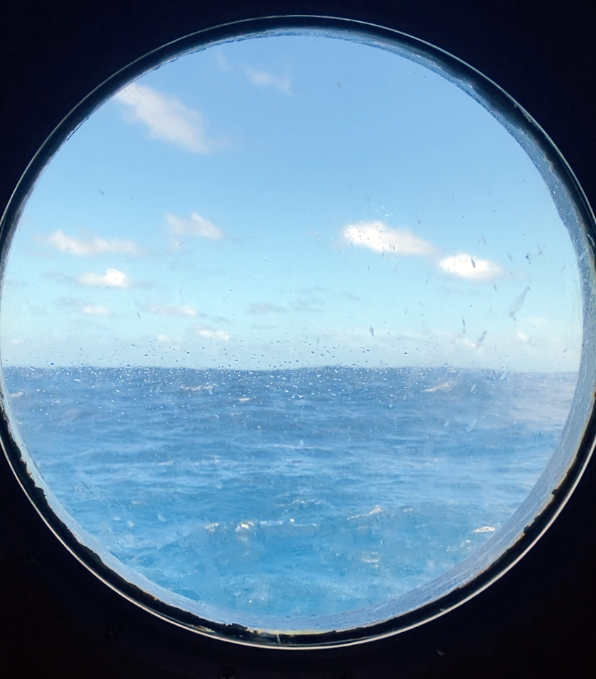 View out a porthole looking out onto blue sky and bright blue sea