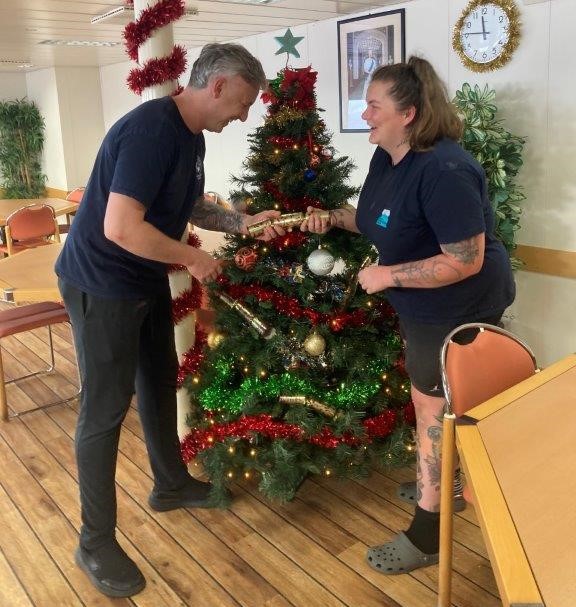 Crew on the RRS James Cook pull a cracker in front of the Christmas tree in the mess, where the crew will share a full traditional turkey roast dinner on Christmas Day. 