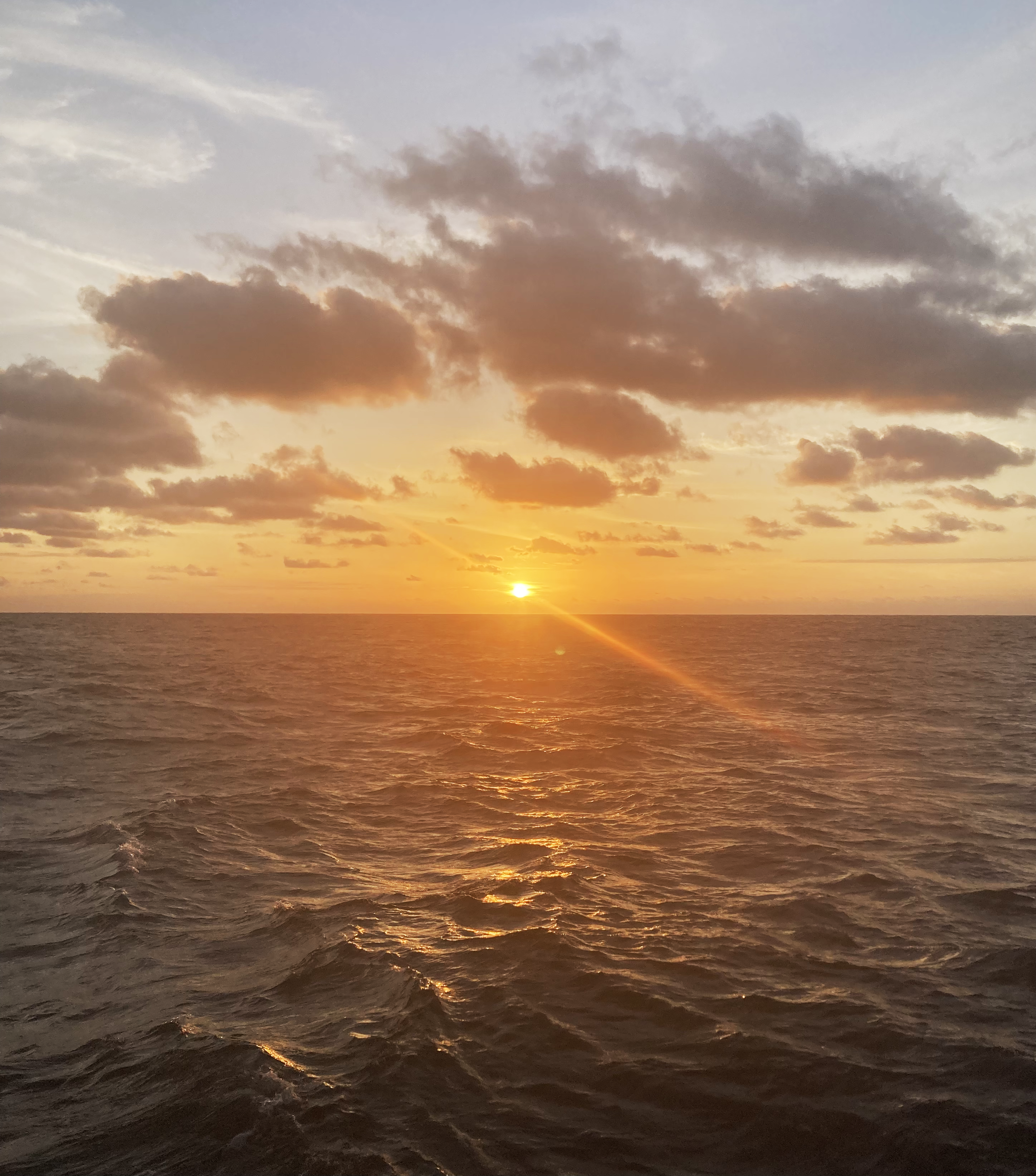 view of a sunrise over a dark sea, scattered grey clouds in the sky